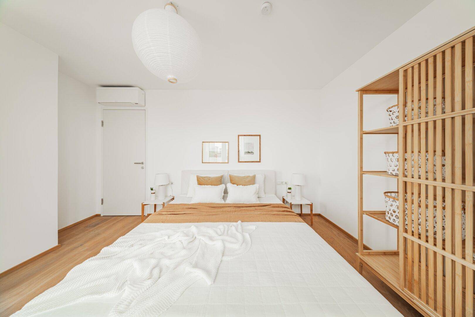Schlafzimmer mit Holzboden, Klimaanlage und modernem Holzregal.