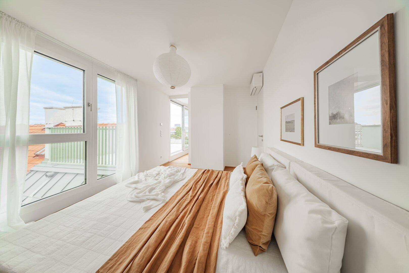 Schlafzimmer mit Holzboden, großen Fenstern und Zugang zu einem Balkon.