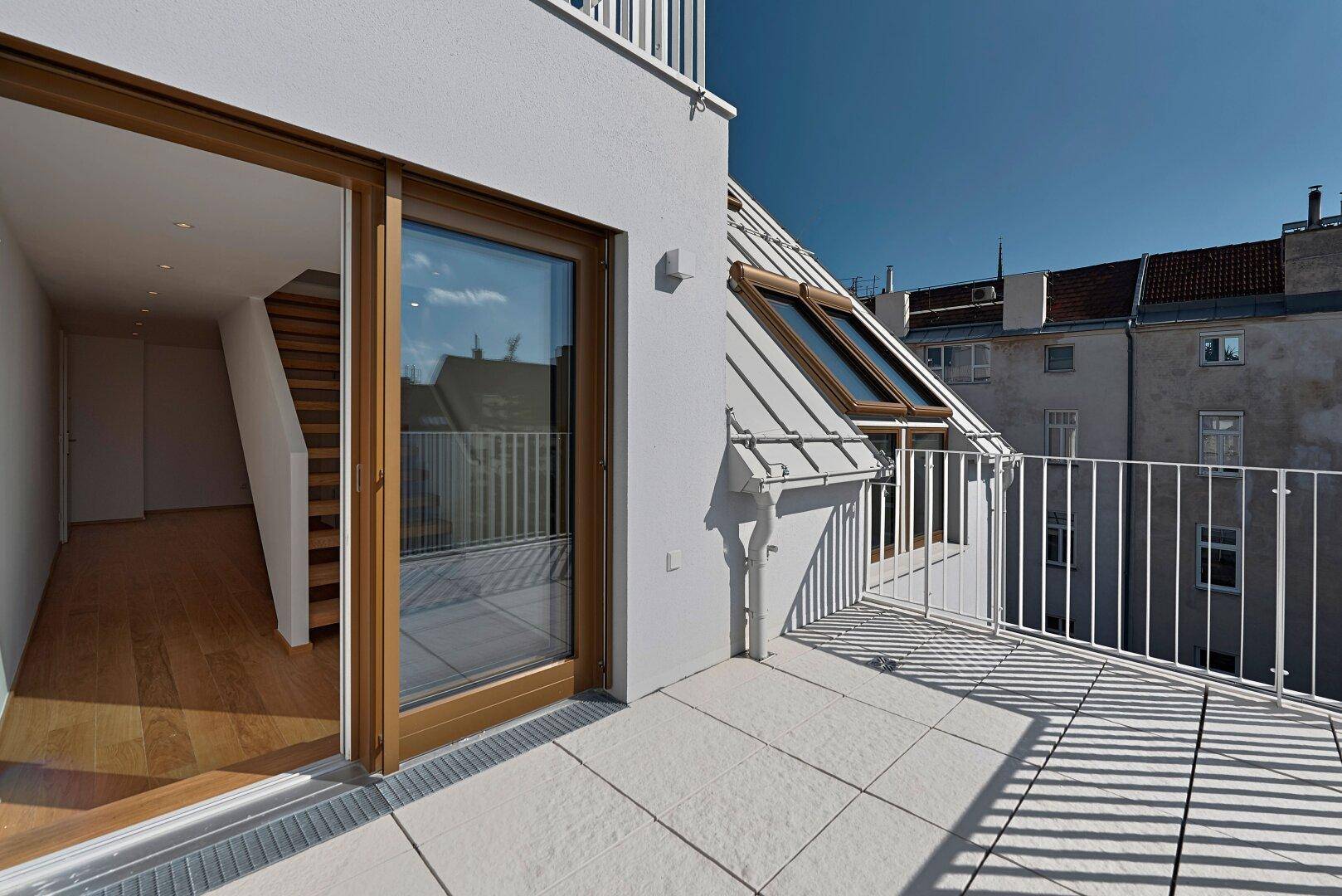 Dachterrasse mit Fliesenboden, Blick auf die Gebäudefassade und Dachfenster.