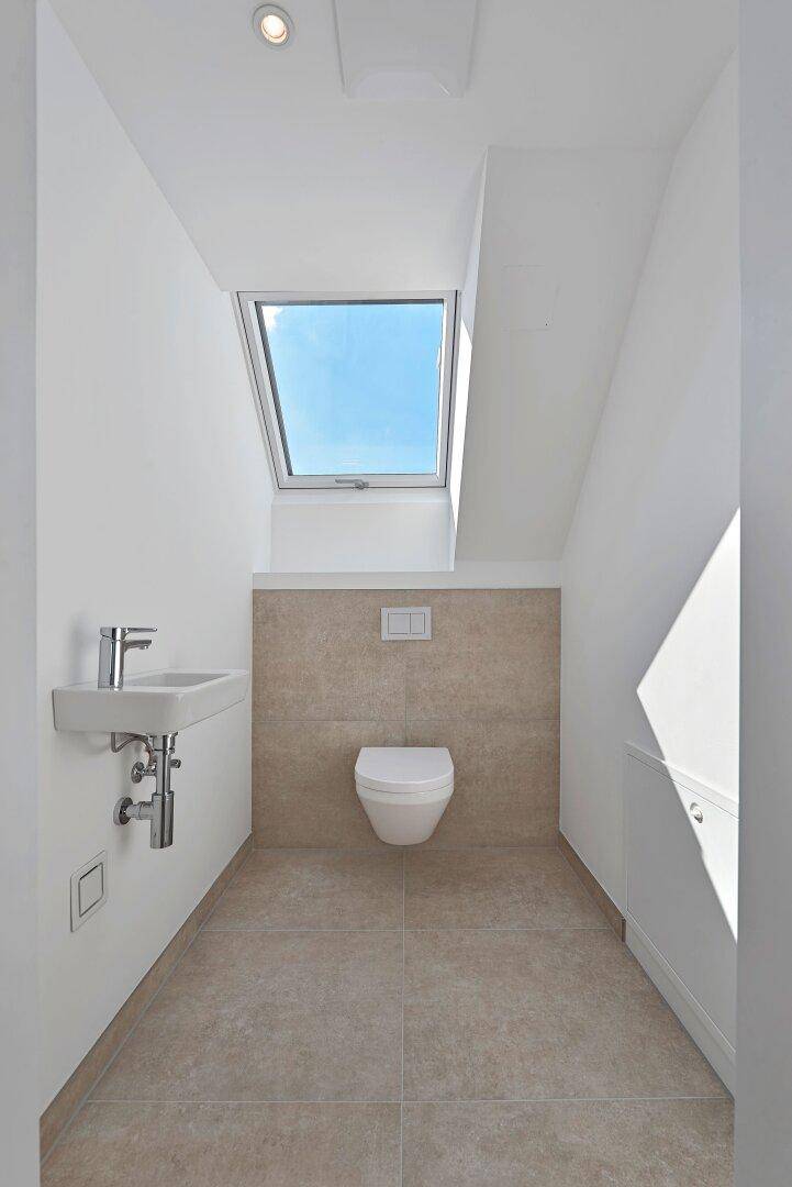 Separates WC mit wandhängender Toilette, kleinem Waschbecken und Dachfenster.