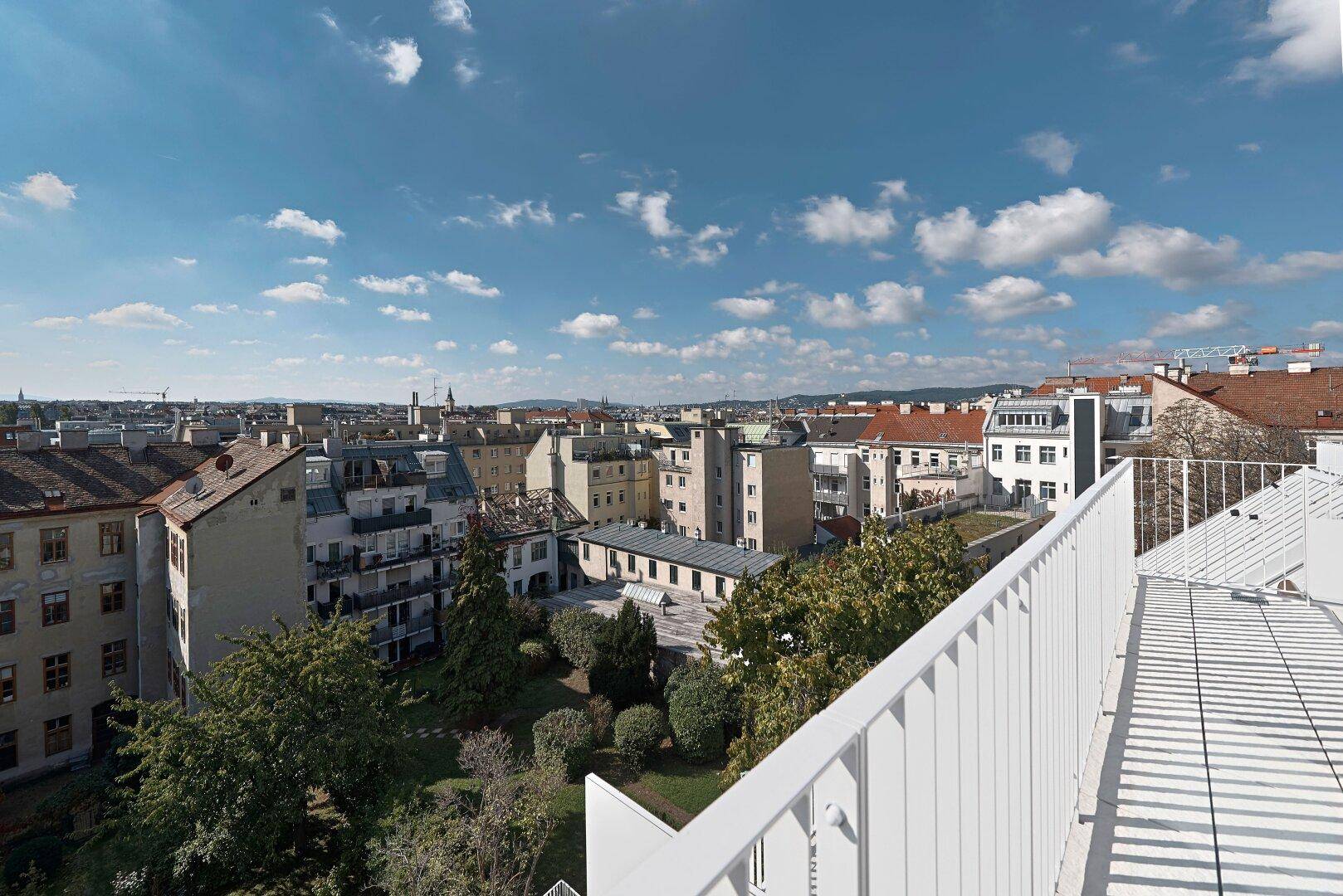 Sonniger Balkon mit weitem Blick über die Stadt und grüne Innenhöfe.