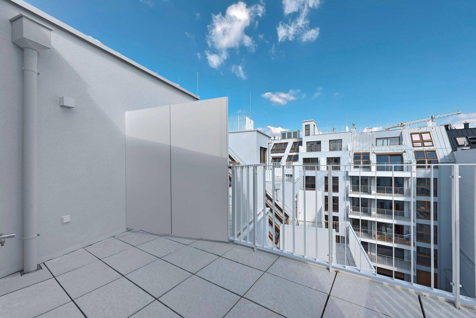 Dachterrasse mit Fliesenboden und Blick auf die moderne Architektur der Nachbargebäude.