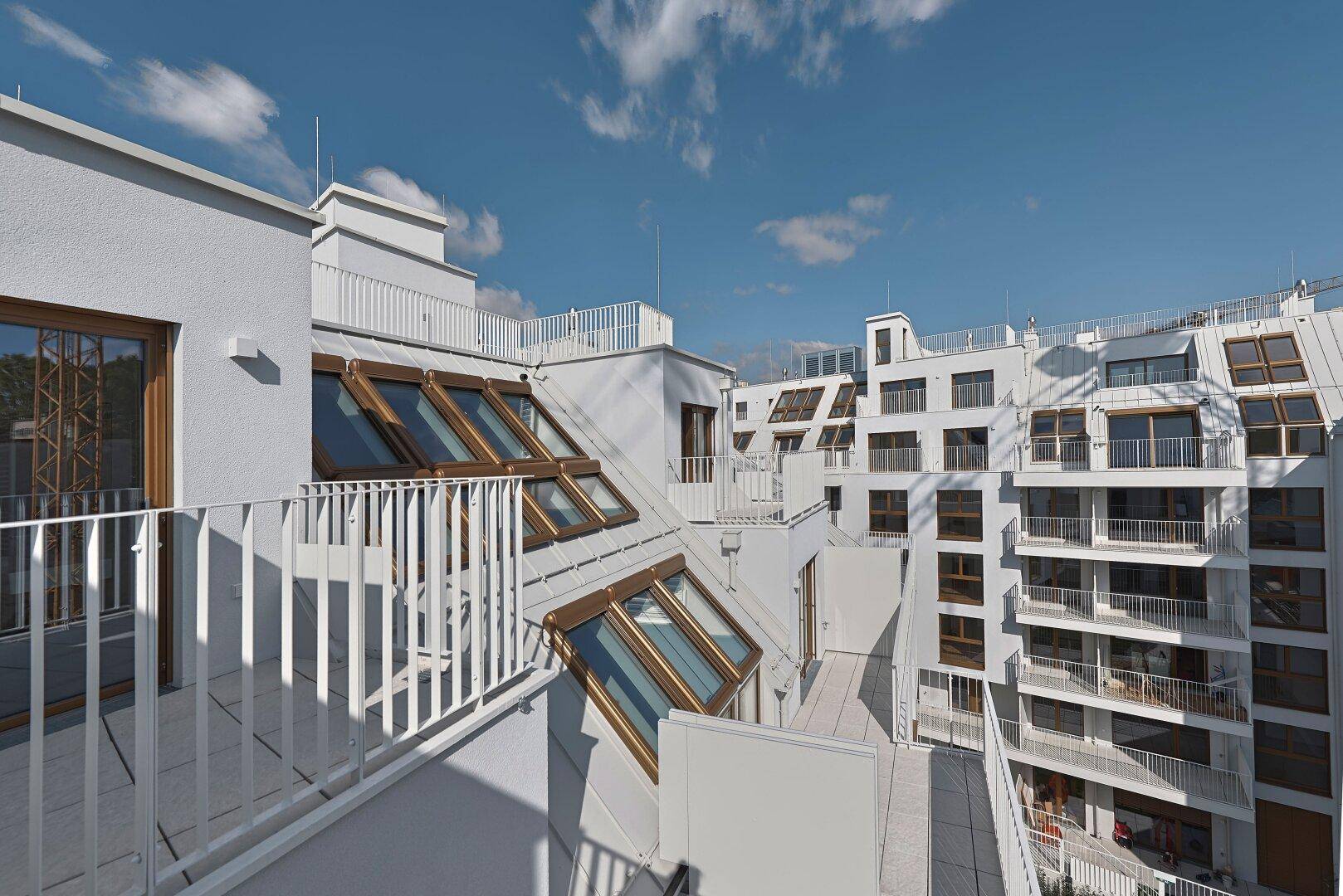 Moderne Architektur mit weißen Fassaden, Dachschrägenfenstern und mehreren Balkonen unter blauem Himmel.