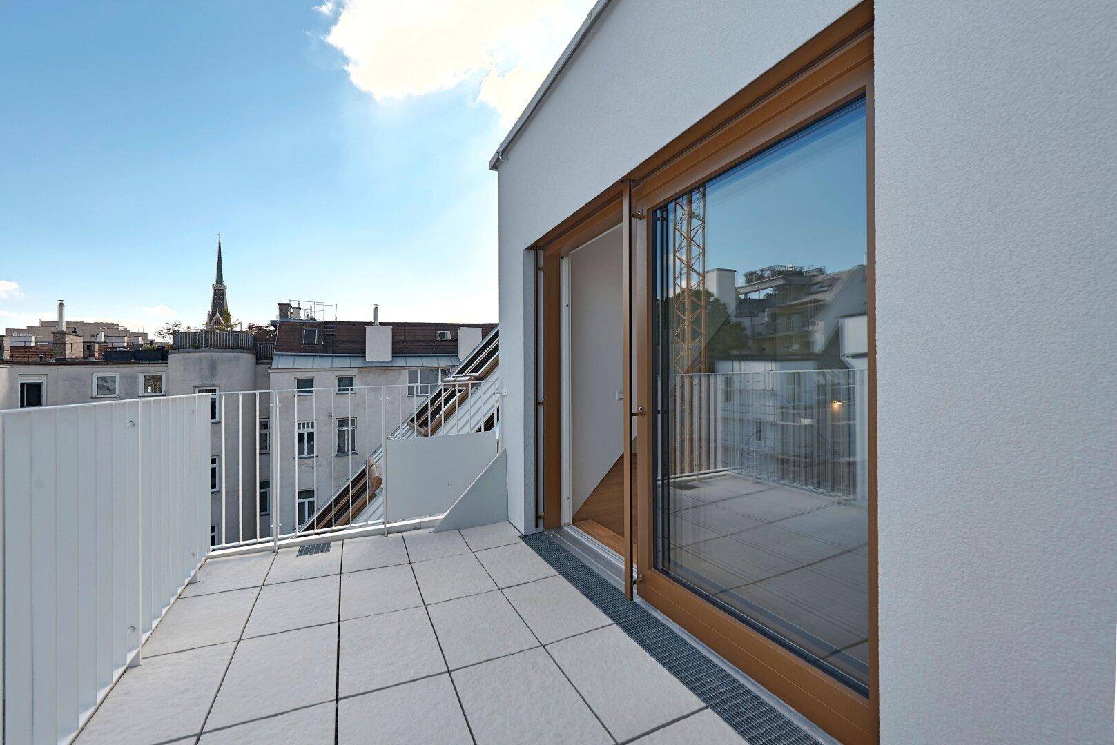 Sonnige Dachterrasse mit Fliesenboden und weitem Blick über die Stadtlandschaft.