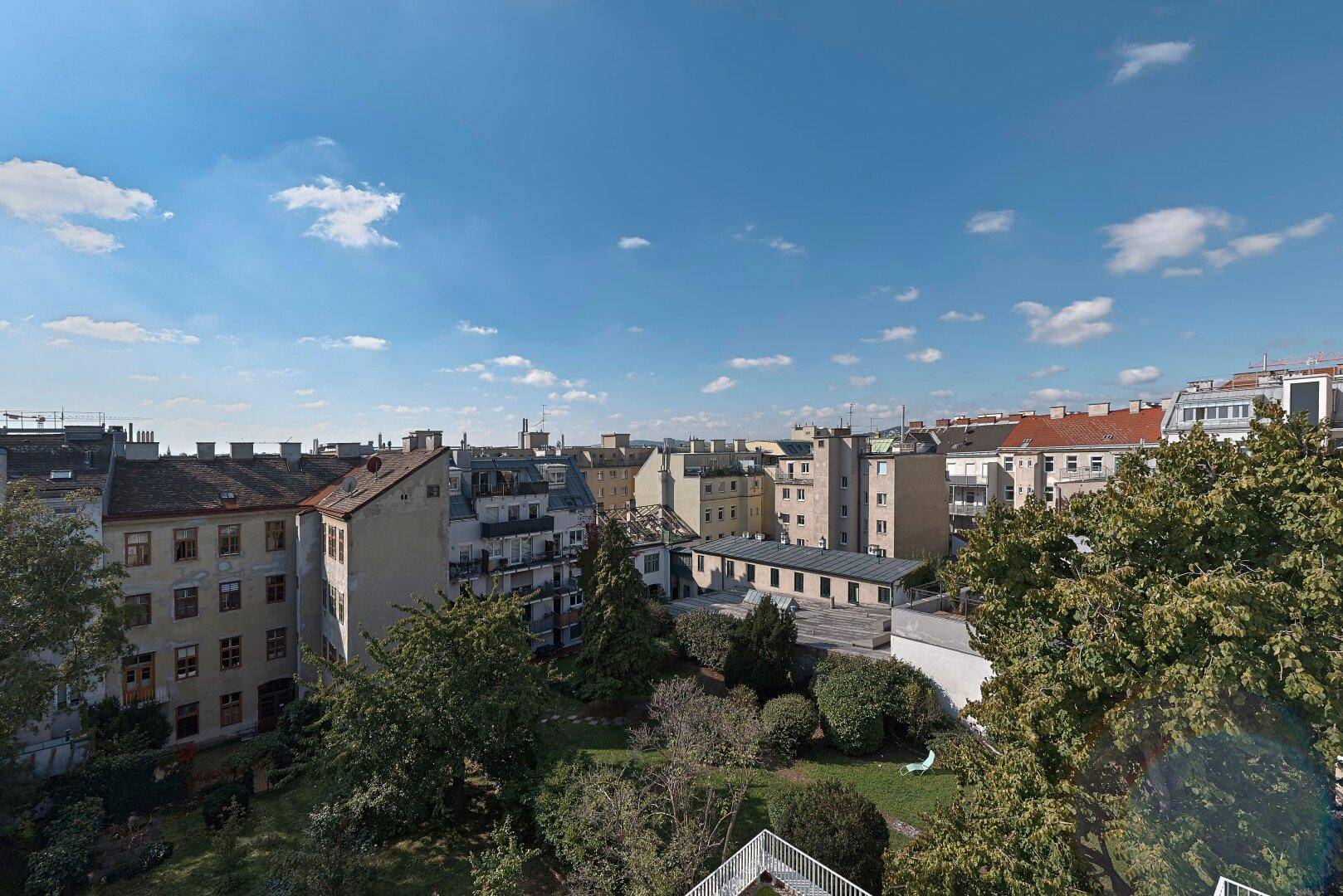 Panoramablick über die Dächer der Stadt mit viel Grün und blauem Himmel.