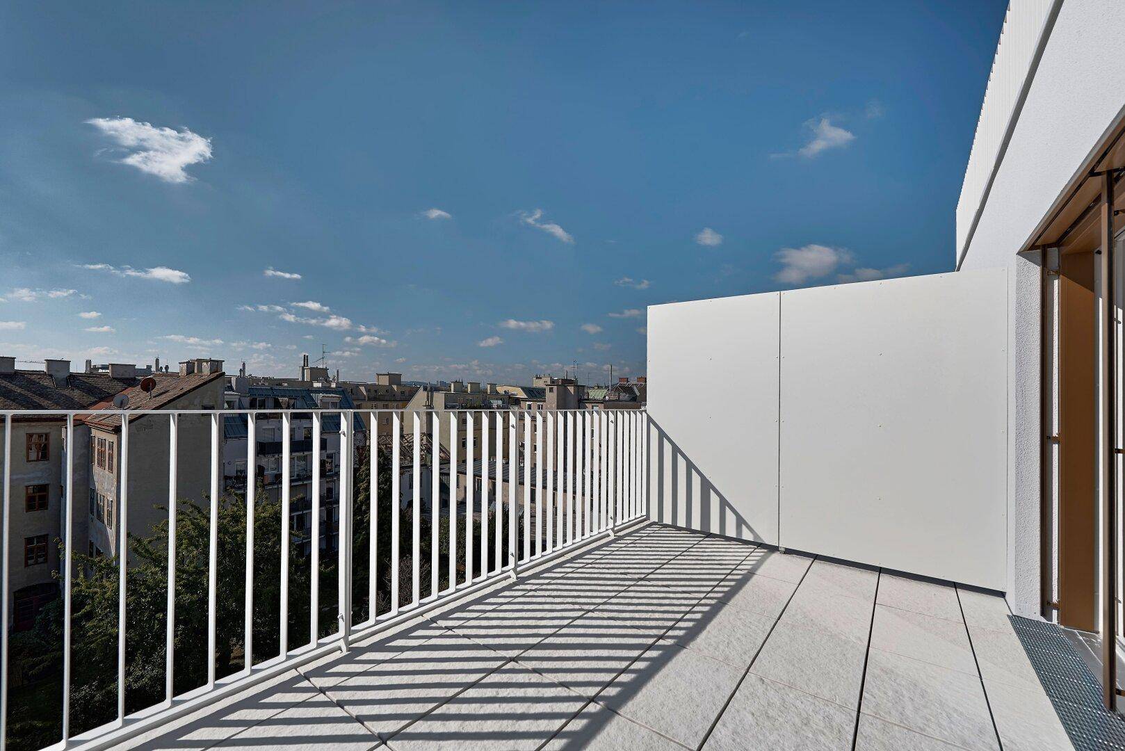 Sonnige Dachterrasse mit weißem Geländer und weitem Blick über die Stadt.