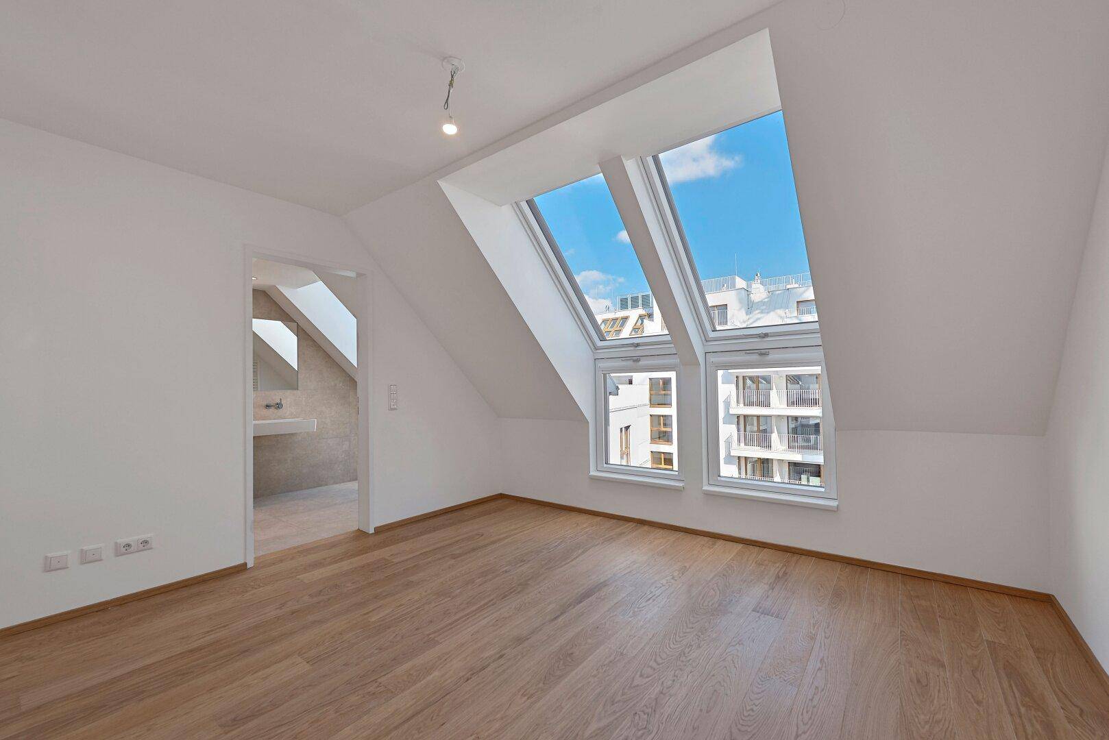 Geräumiges Schlafzimmer mit Holzboden, Dachfenstern und Blick in ein angrenzendes Bad.