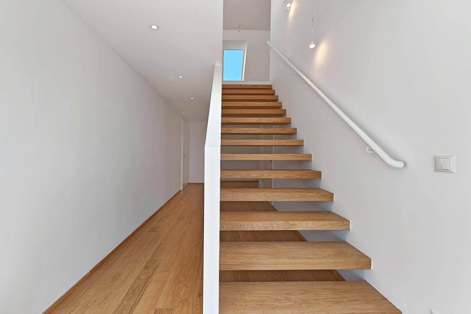 Elegante Holztreppe mit schwebenden Stufen und Handlauf in einem hellen Flur.