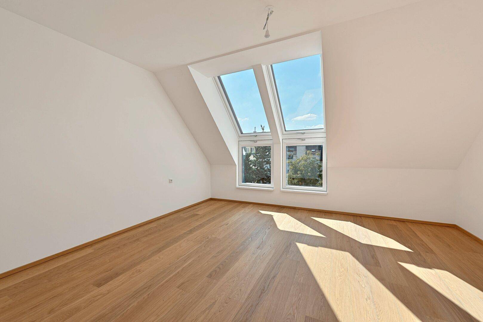 Helles Schlafzimmer mit Holzboden, Dachschräge und großen Dachfenstern für viel Licht.