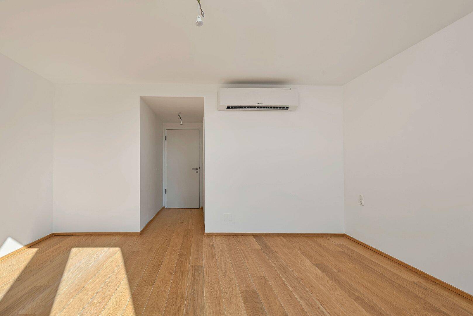 Ruhiges Schlafzimmer mit Holzboden, Klimaanlage und weiß gestrichenen Wänden.