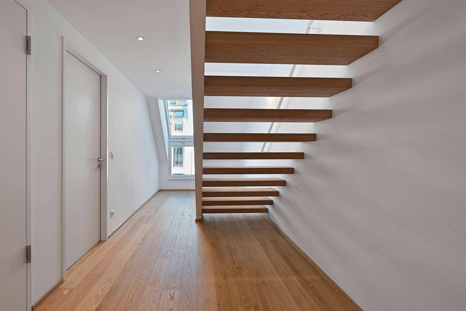 Moderner Flur mit Holzboden und einer eleganten, freitragenden Holztreppe, die die Etagen verbindet.