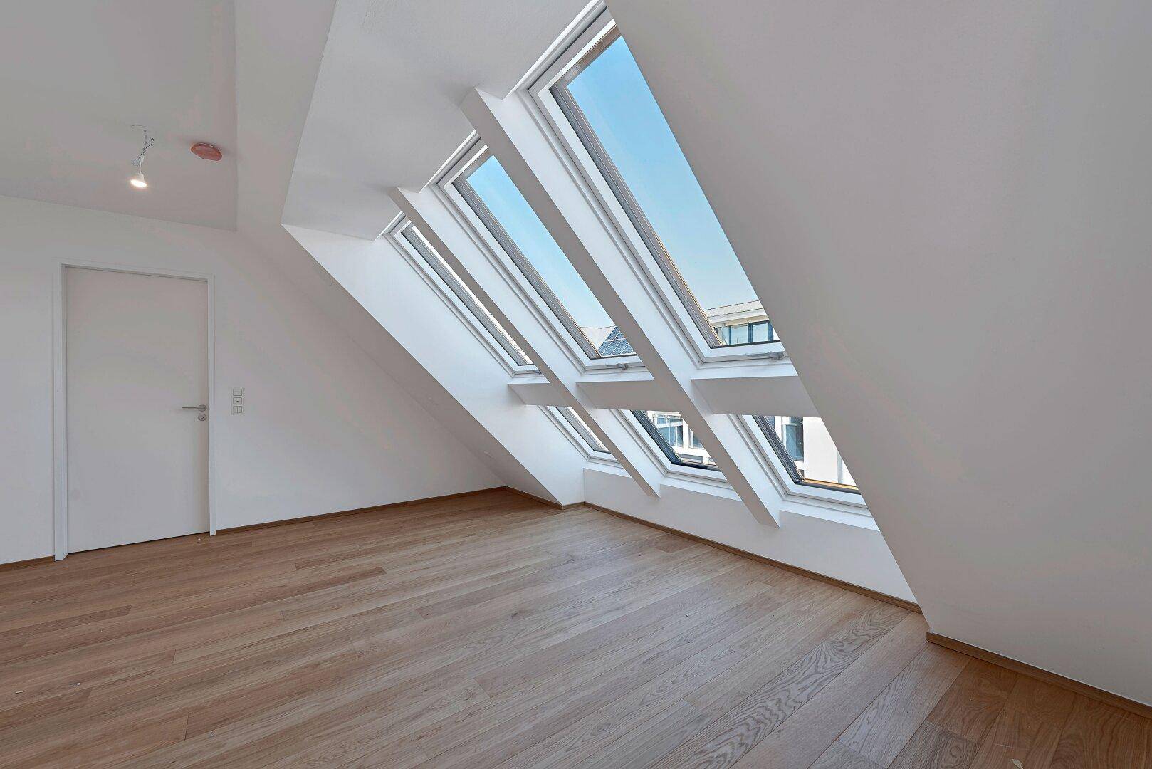 Helles Dachgeschosszimmer mit Holzboden, weißen Wänden und mehreren schrägen Dachfenstern.