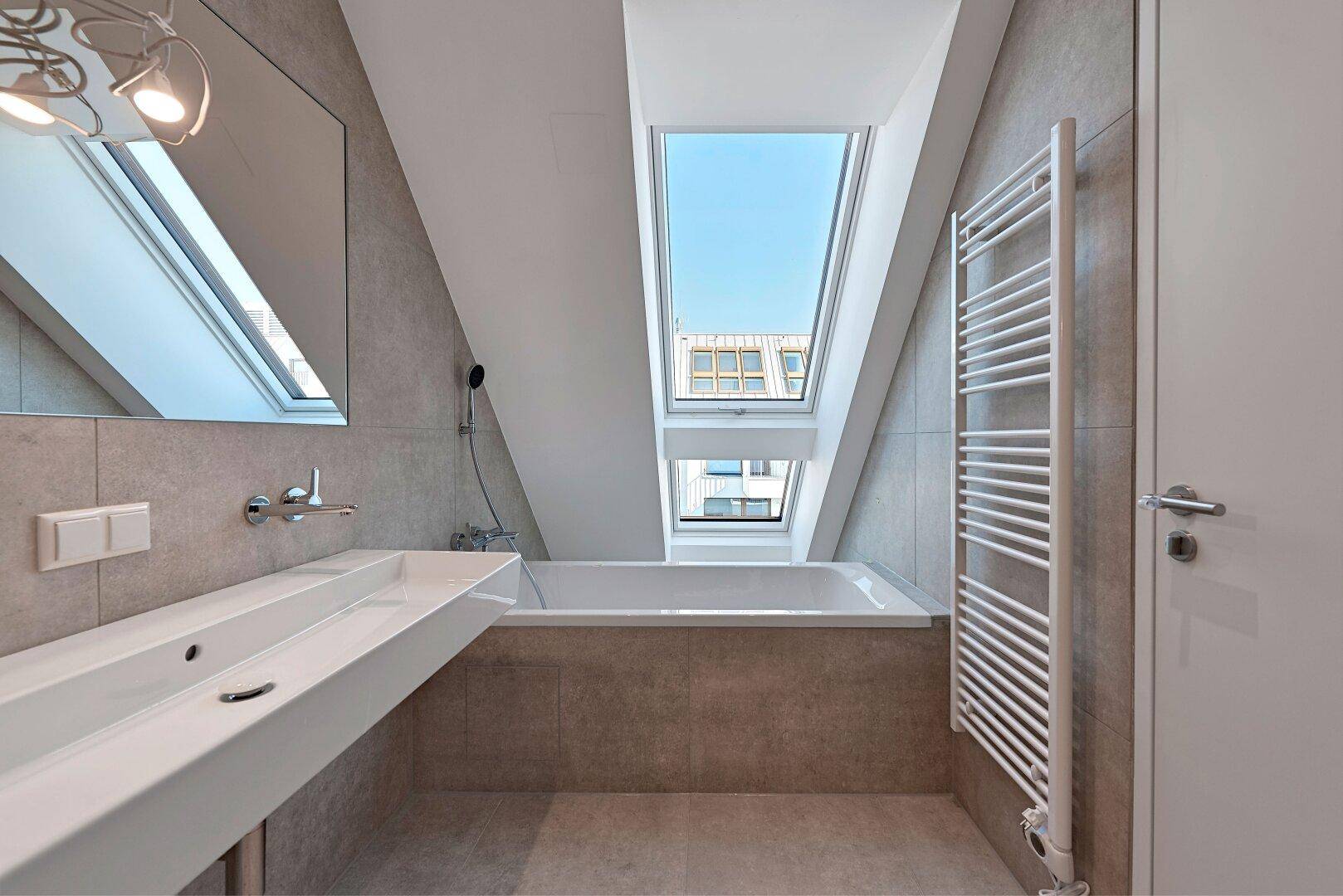 Helles Badezimmer mit Badewanne, Einzelwaschbecken, beheiztem Handtuchhalter und Dachfenstern.