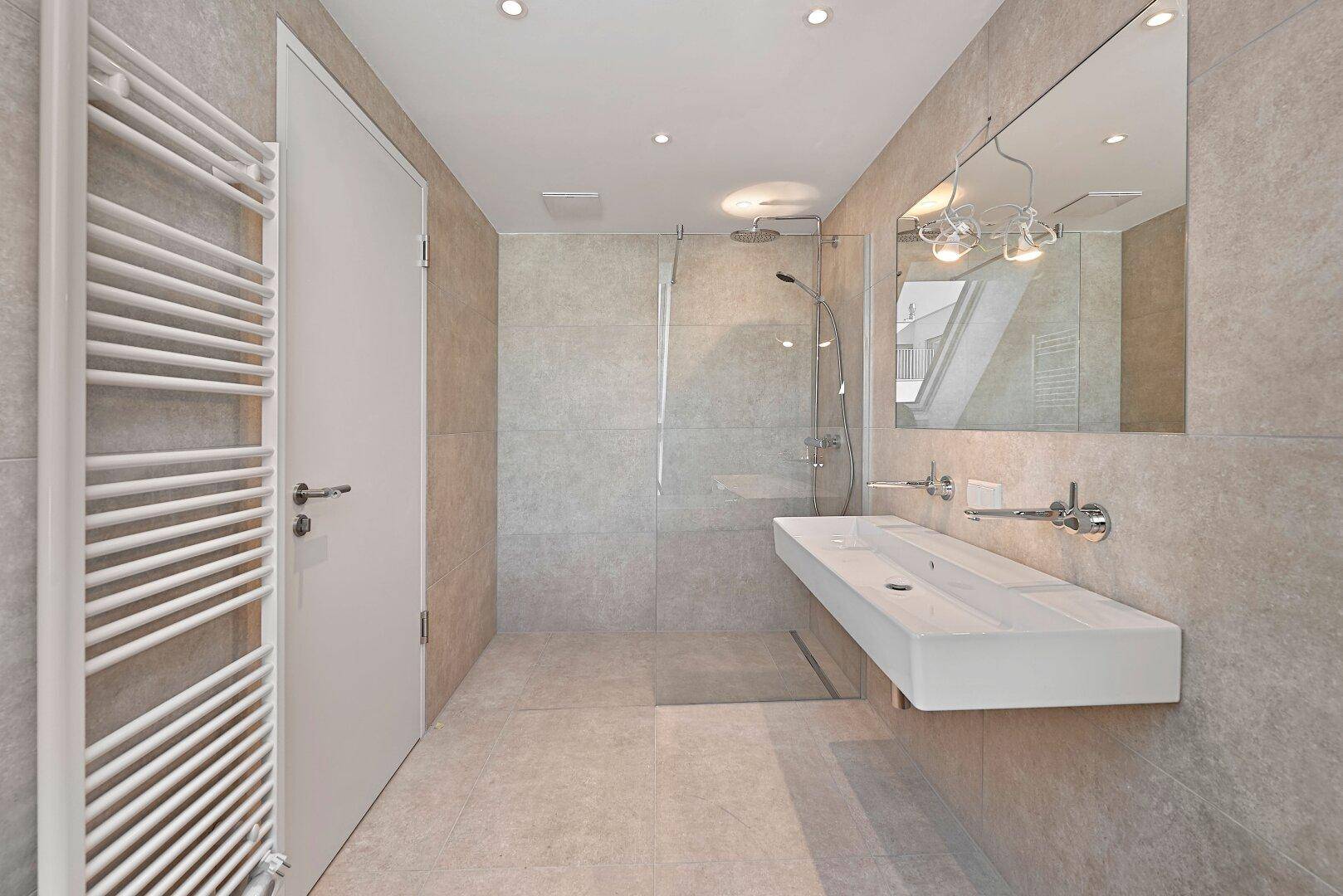 Modernes Badezimmer mit großen grauen Fliesen, begehbarer Dusche und Doppelwaschbecken.