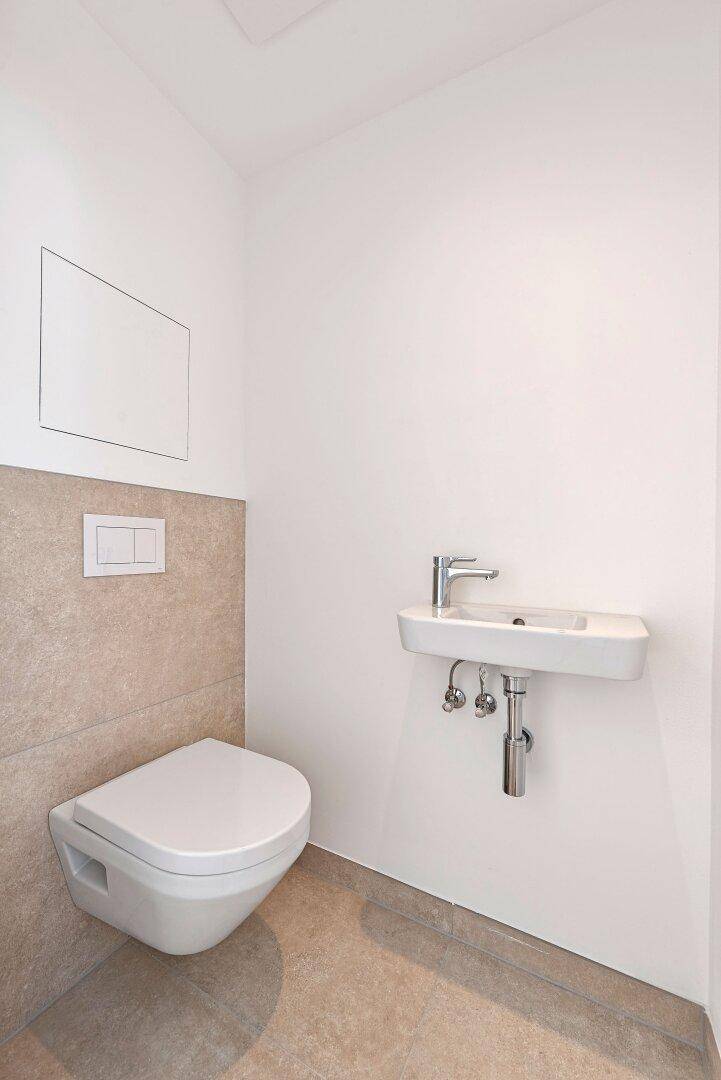 Modernes Gäste-WC mit wandhängender Toilette und kleinem Waschbecken, halbhoch gefliest.