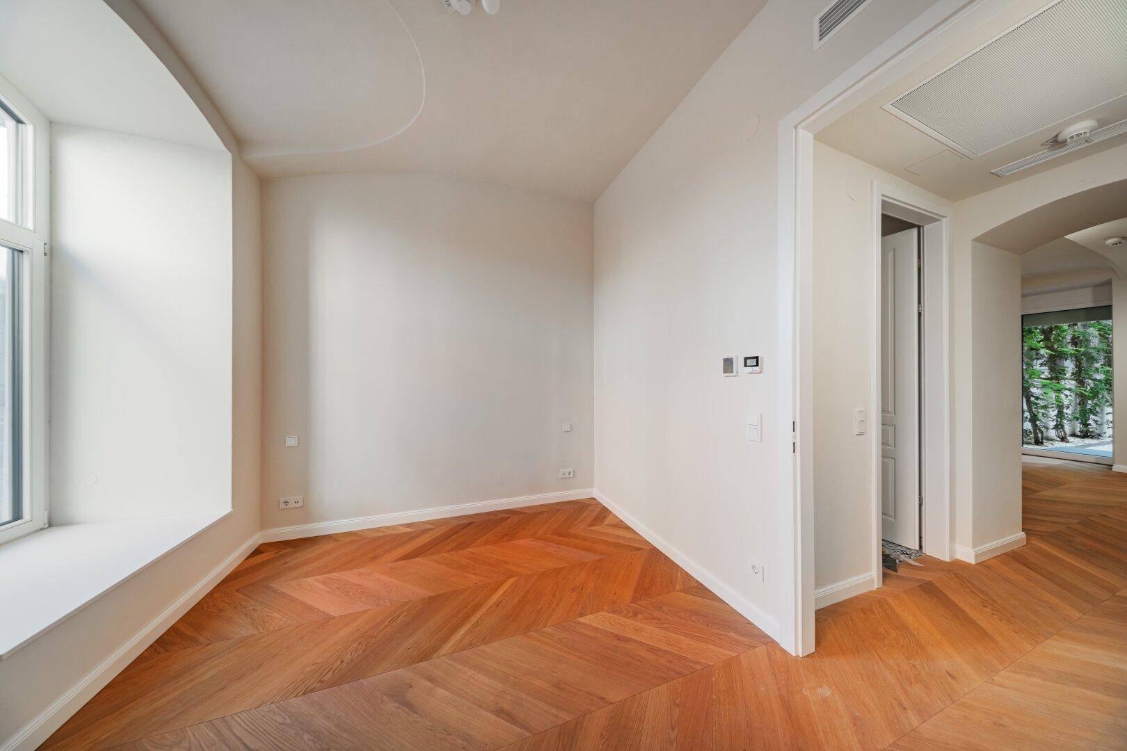 Geräumiges Zimmer mit Fischgrätparkett und Zugang zu einem Außenbereich.