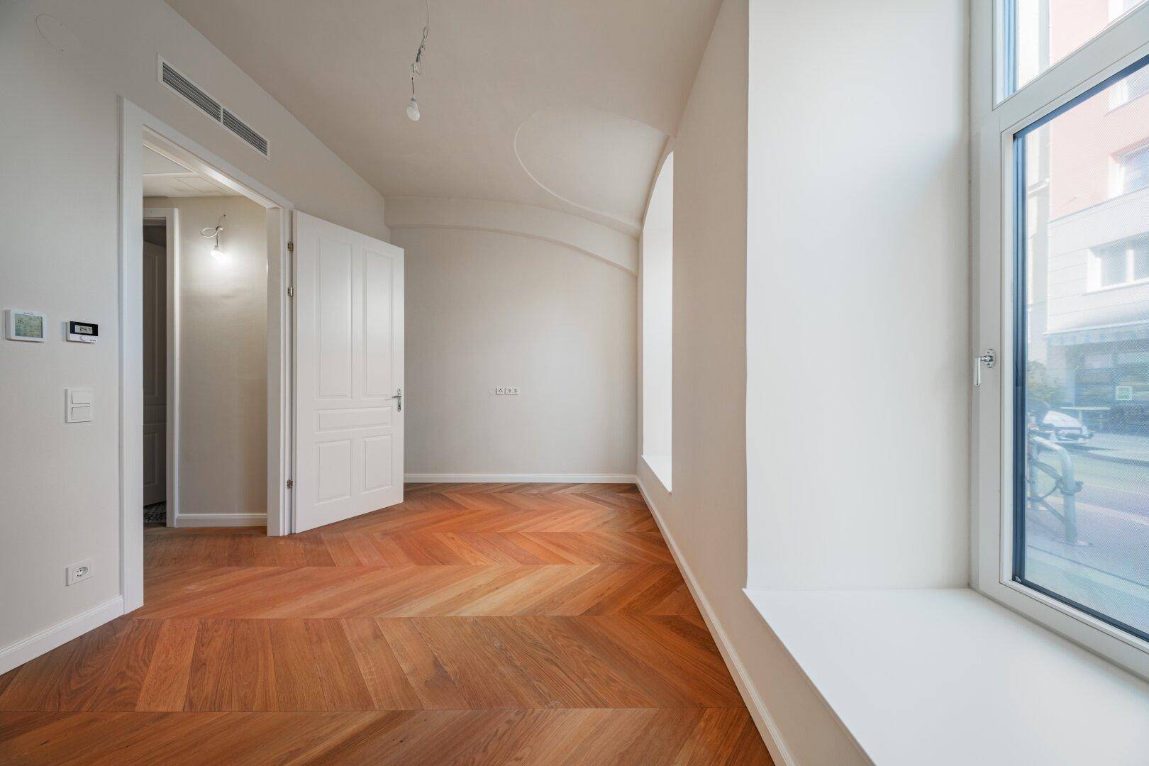 Helles Zimmer mit Fischgrätparkett und einem großen Fenster mit breiter Fensterbank.