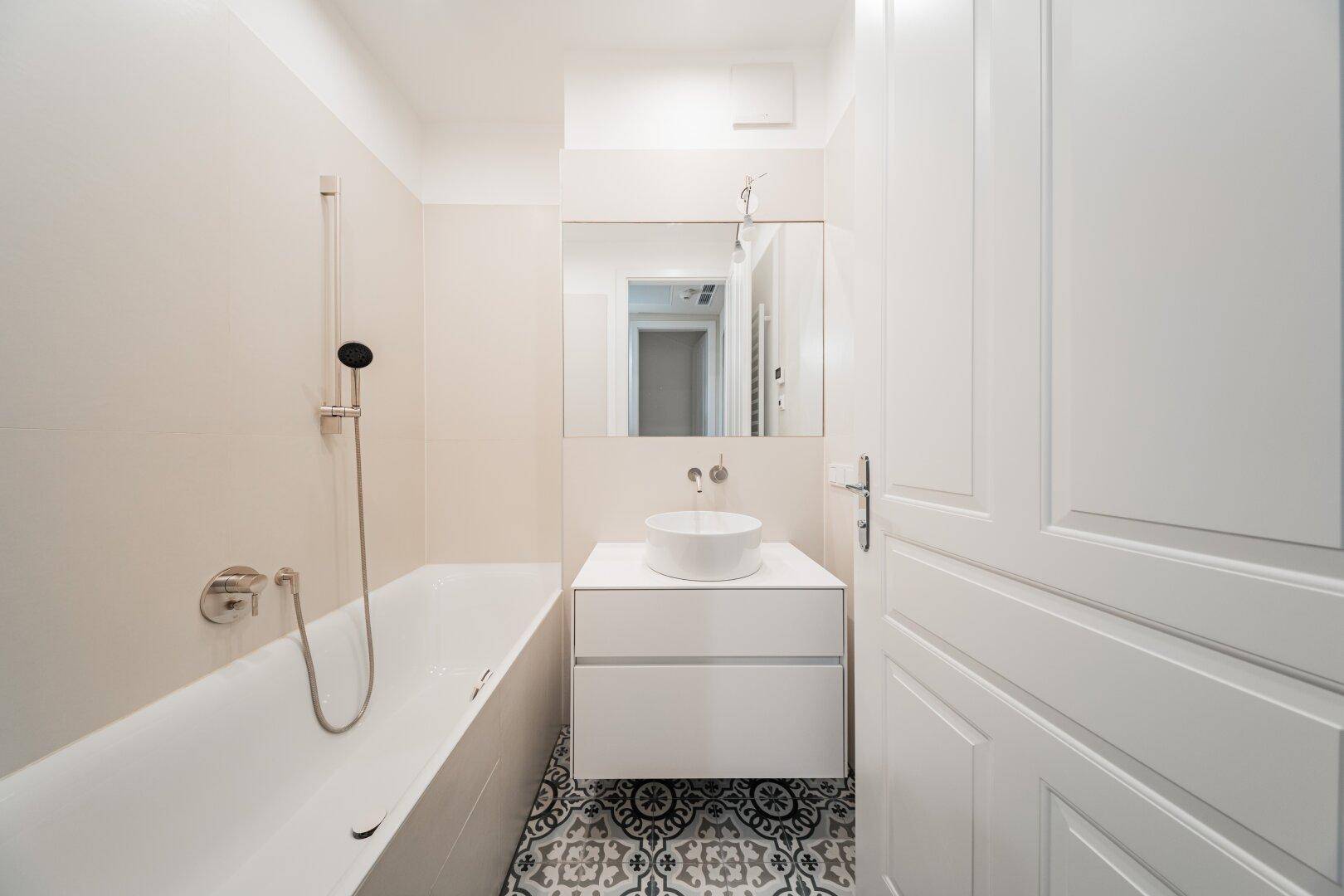 Modernes Badezimmer mit Badewanne, Aufsatzwaschbecken und gemusterten Bodenfliesen.