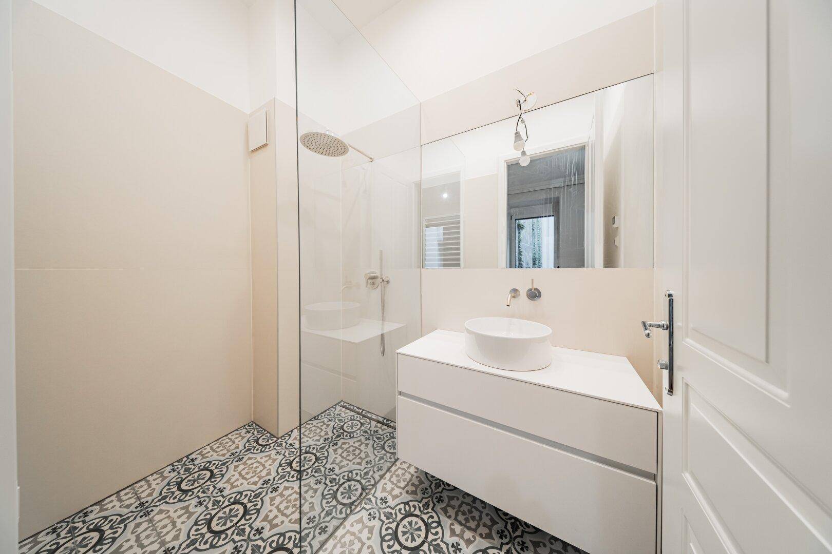 Modernes Badezimmer mit begehbarer Dusche, Aufsatzwaschbecken und gemusterten Fliesen am Boden.