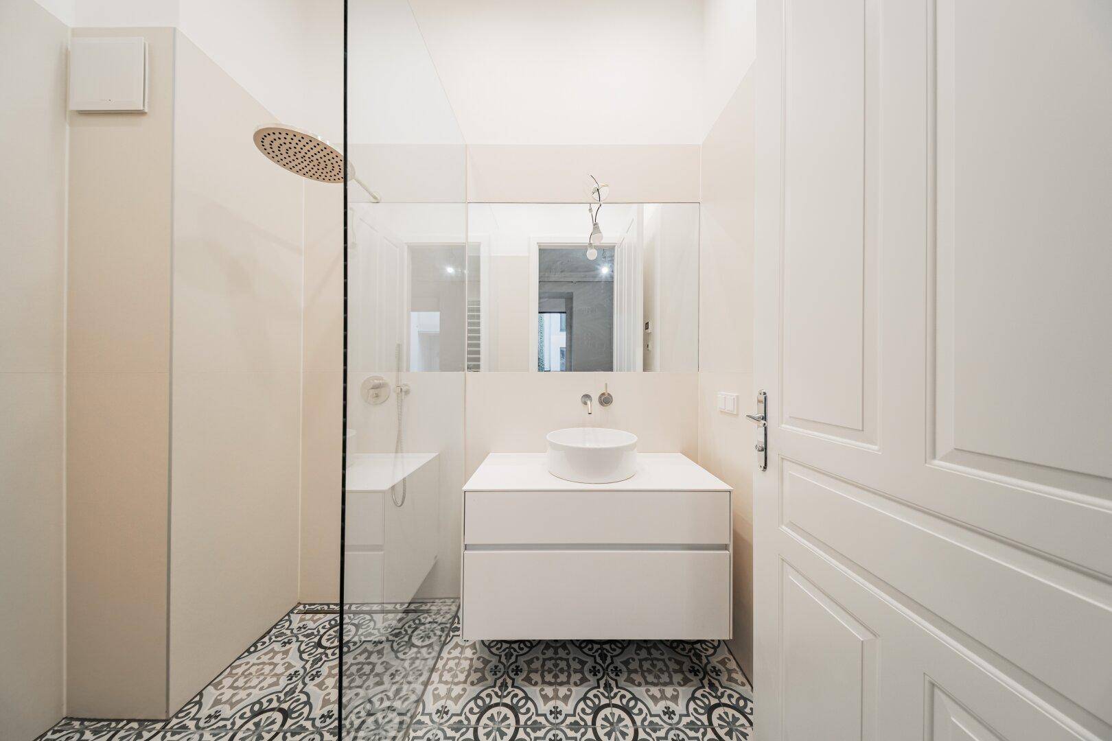 Stilvolles Badezimmer mit begehbarer Dusche, großem Spiegel und gemustertem Fliesenboden, sehr gepflegt.