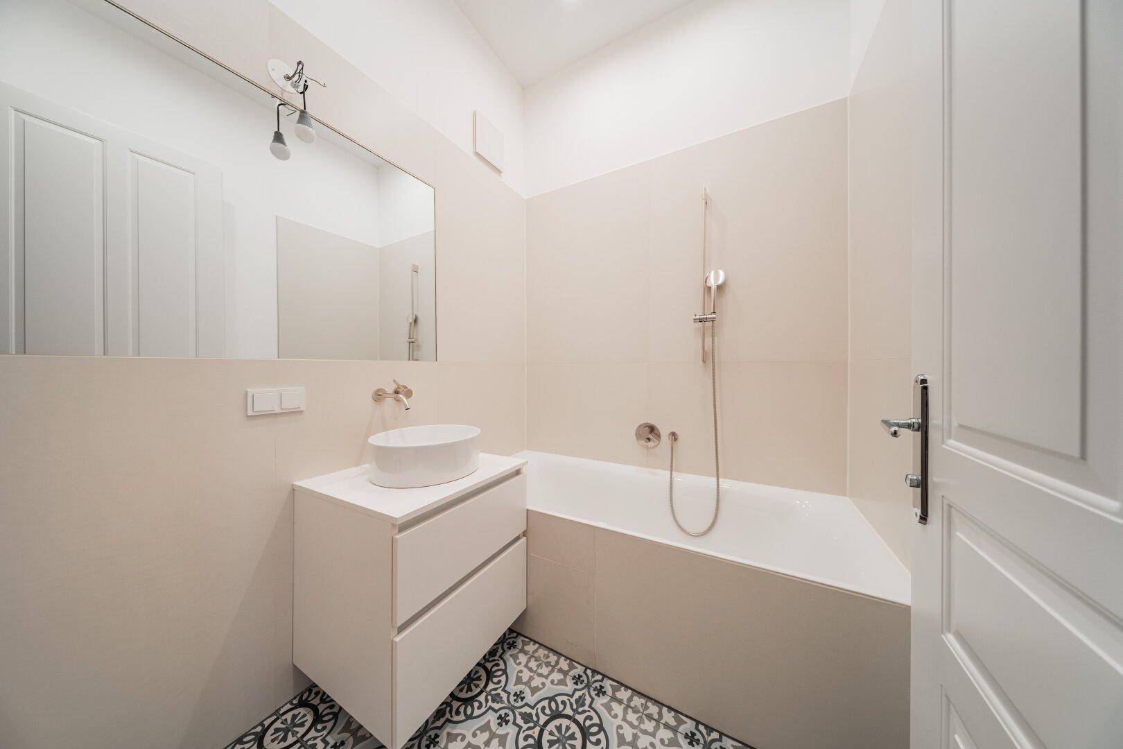 Elegantes Badezimmer mit Badewanne, modernem Waschtisch und gemusterten Bodenfliesen, hell und funktional.