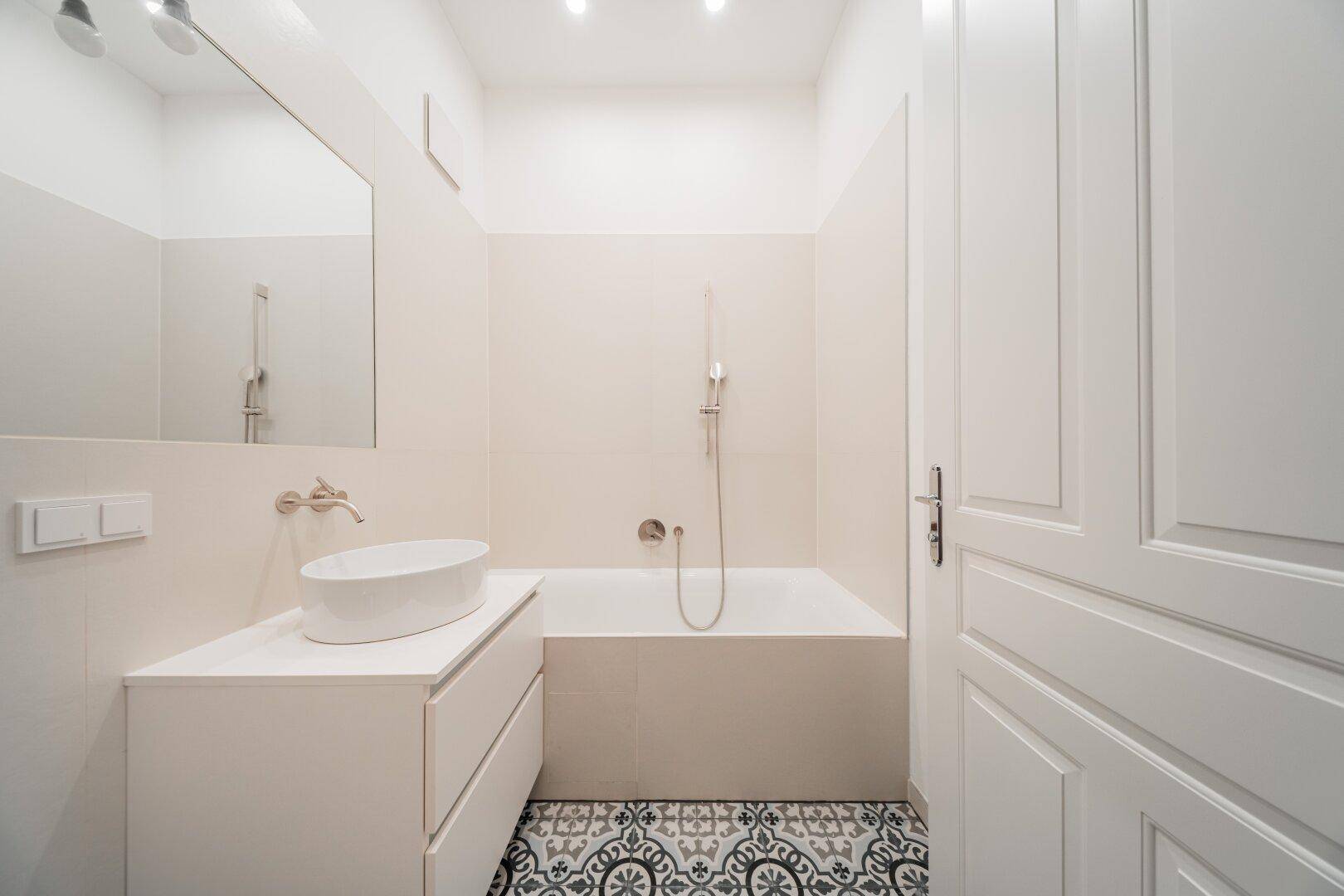 Stilvolles Badezimmer mit Badewanne, modernem Aufsatzwaschbecken und dekorativen Bodenfliesen, frisch renoviert.