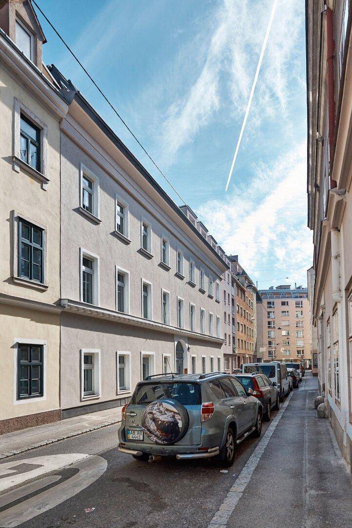 Blick auf eine ruhige Stadtstraße mit parkenden Autos und der historischen Gebäudefassade.