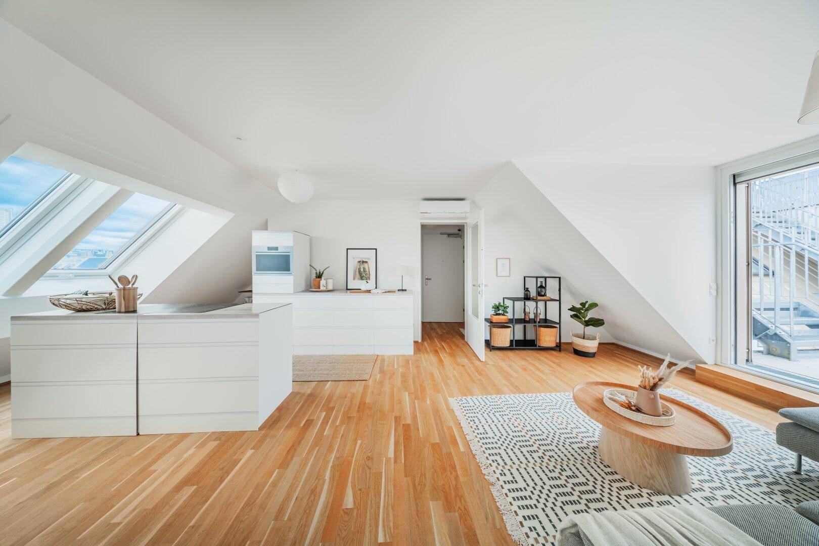 Offener Wohnbereich mit Kücheninsel, Holzboden und Zugang zu einer Dachterrasse.