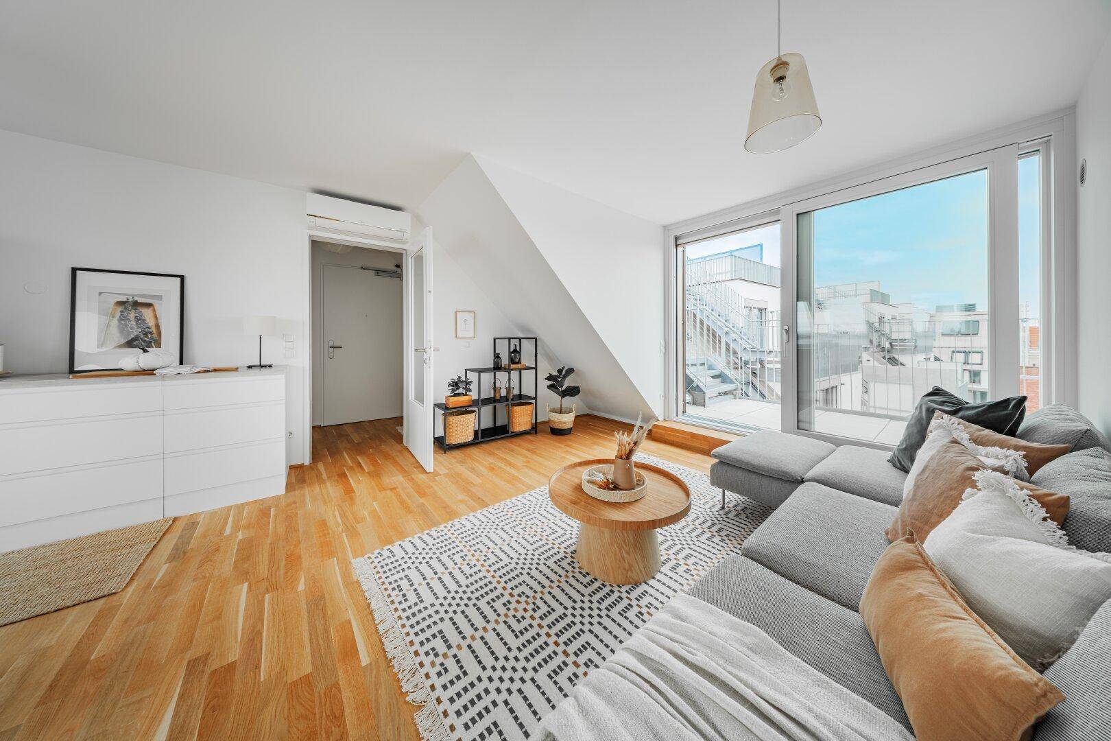 Helles Wohnzimmer mit Holzboden, Dachschräge und Zugang zu einer Außenterrasse.