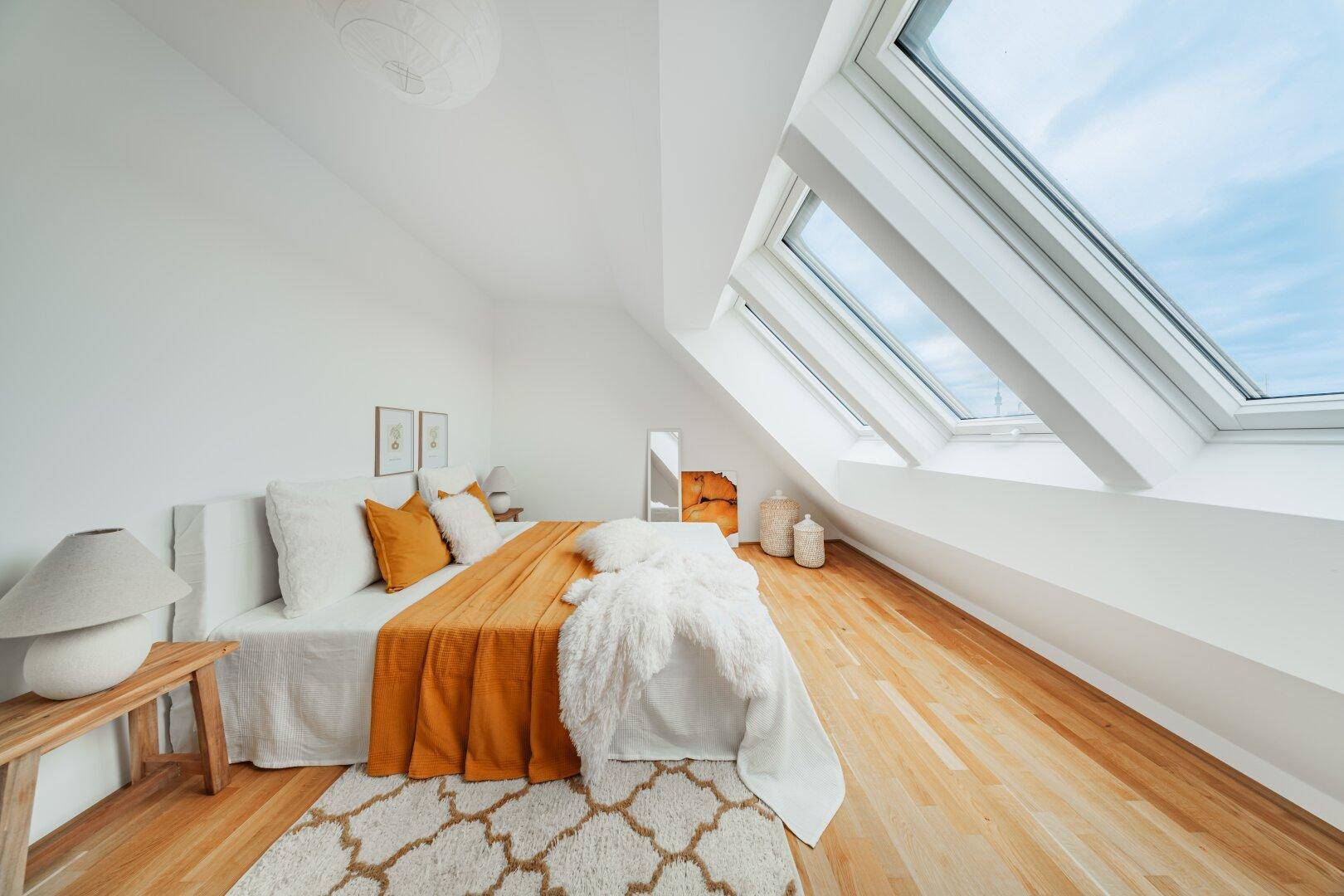 Helles Schlafzimmer mit Holzboden, Dachschräge und drei großen Dachfenstern.