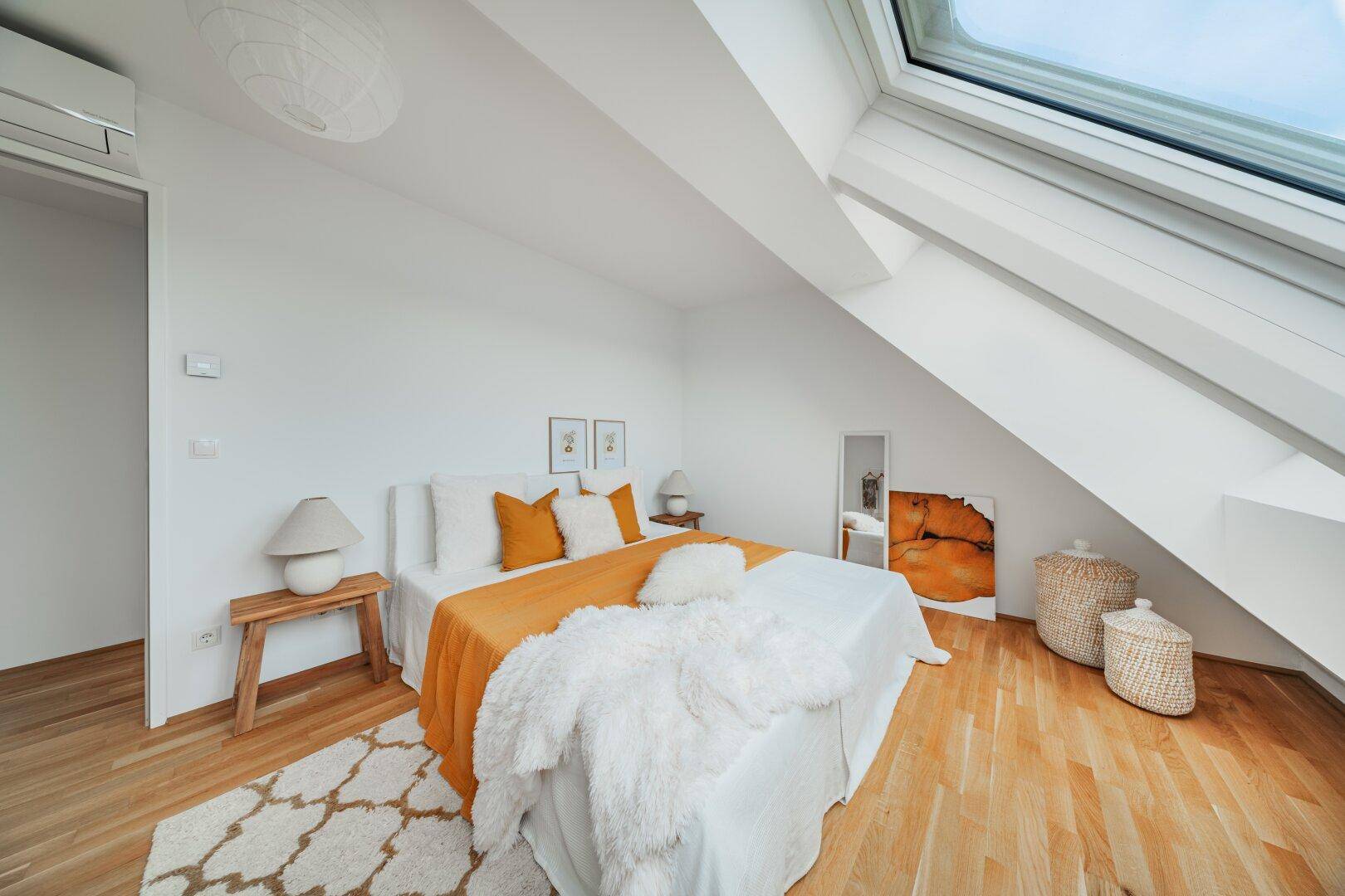 Schlafzimmer mit Holzboden, Dachschräge, Klimaanlage und viel Tageslicht durch Dachfenster.