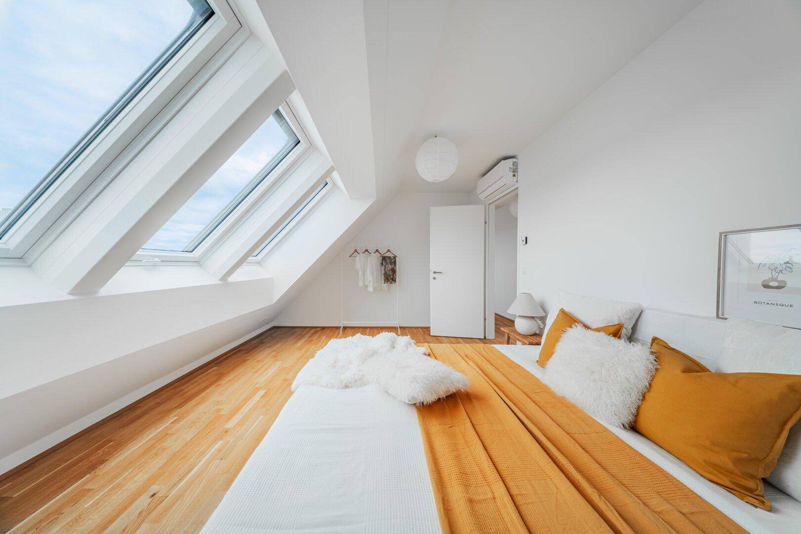 Geräumiges Schlafzimmer mit Holzboden, Dachschräge und hellen Dachfenstern.