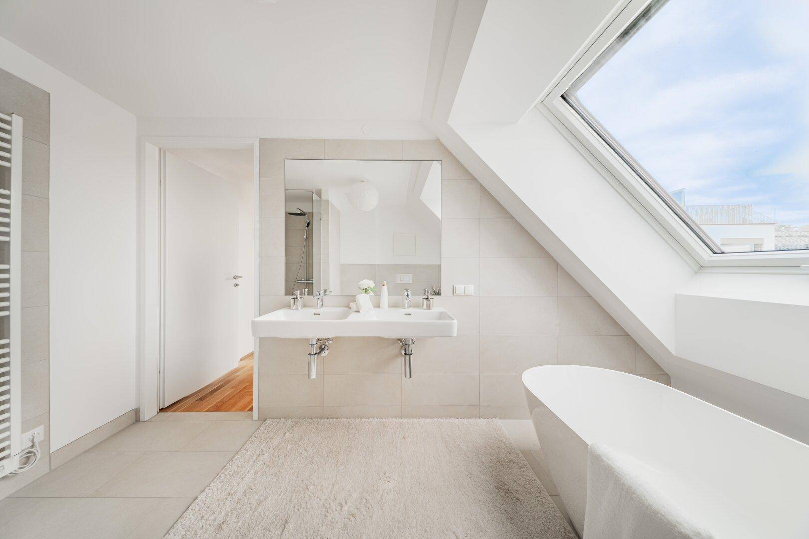 Modernes Badezimmer mit Doppelwaschbecken, freistehender Badewanne und Dachfenster.