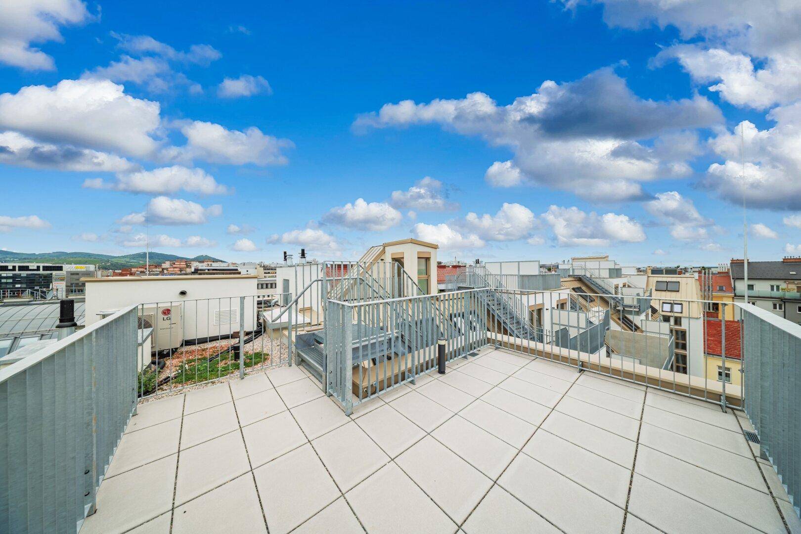Weitläufige Dachterrasse mit Metallgeländer und Panoramablick über die Stadtlandschaft.