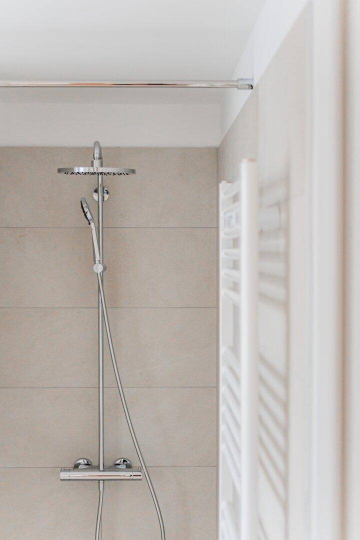 Moderne Regendusche und beheizter Handtuchhalter in einem hellen Badezimmer.