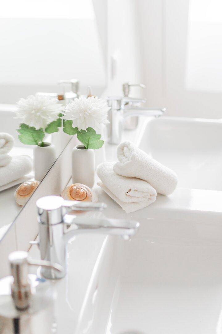 Doppelwaschbecken mit modernen Armaturen und dekorativen Blumen im Badezimmer.