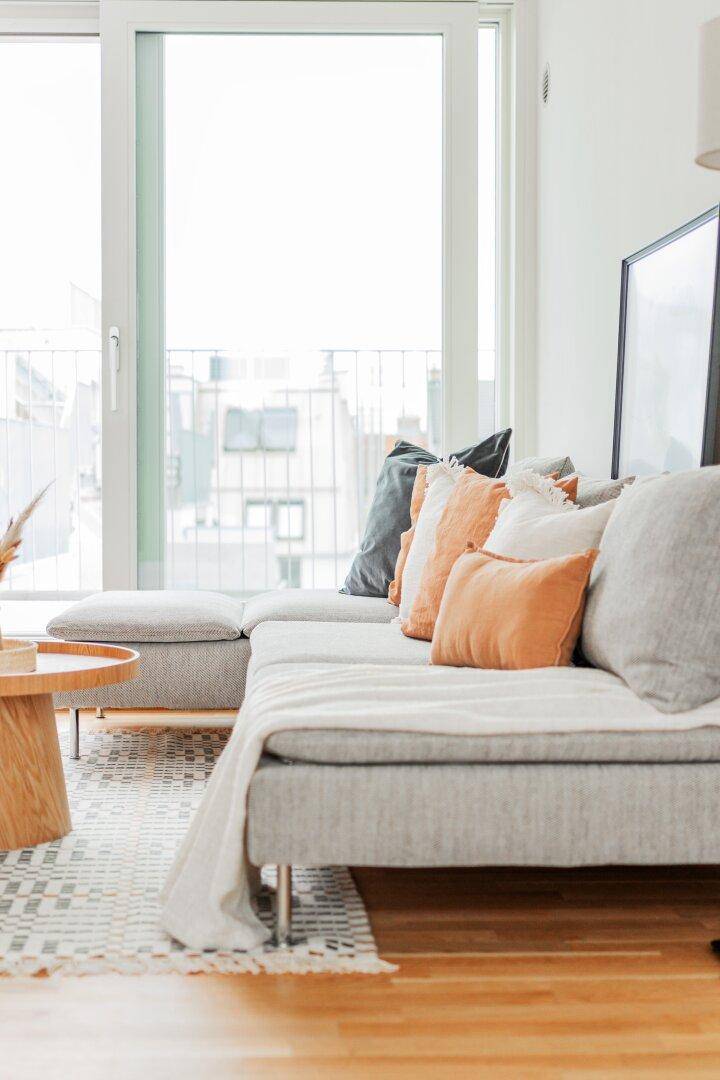 Gemütliches Ecksofa mit farbigen Kissen und Blick auf die Terrasse durch große Fenster.