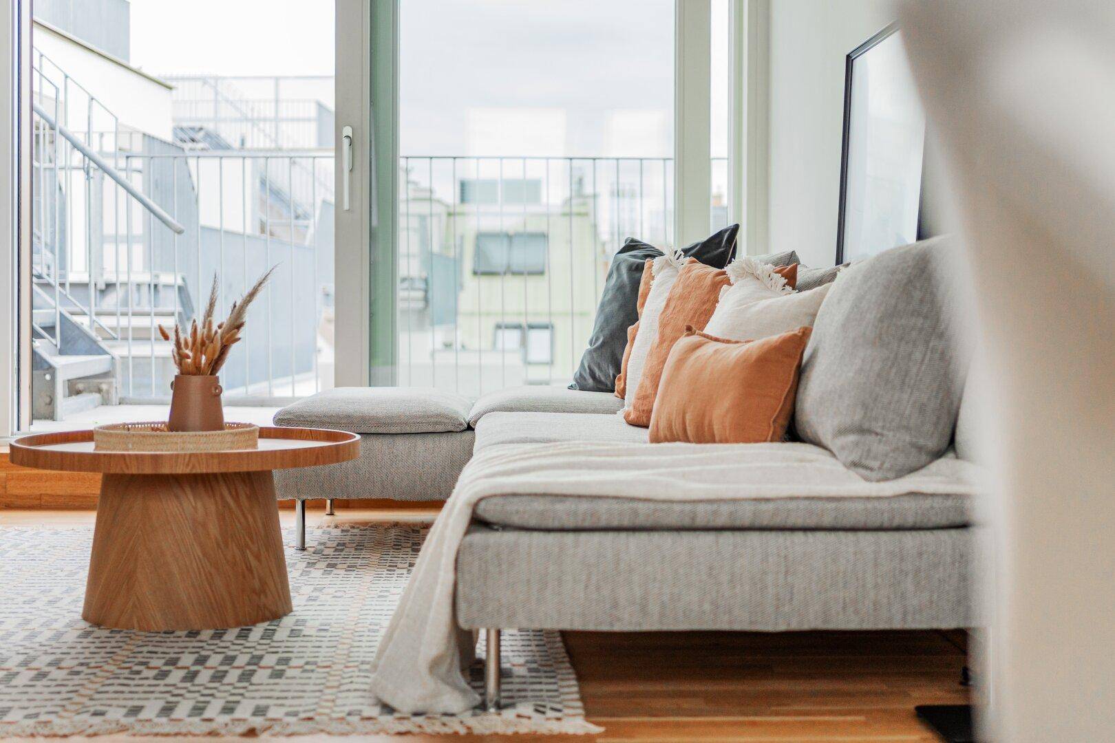 Ecksofa mit Holztisch und Zugang zur Terrasse durch eine große Glasschiebetür.