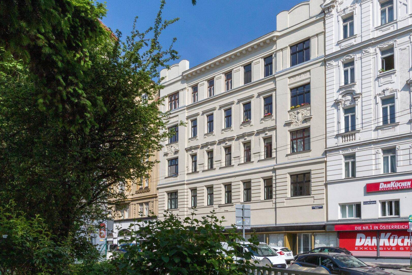 Historisches Gebäude mit klassischer Fassade und Geschäften im Erdgeschoss an einer belebten Straße.