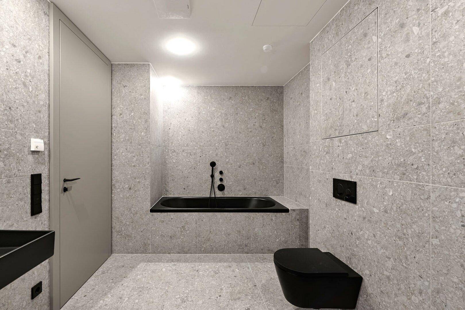 Elegantes Badezimmer mit grauen Fliesen, schwarzer Badewanne und modernem Design.