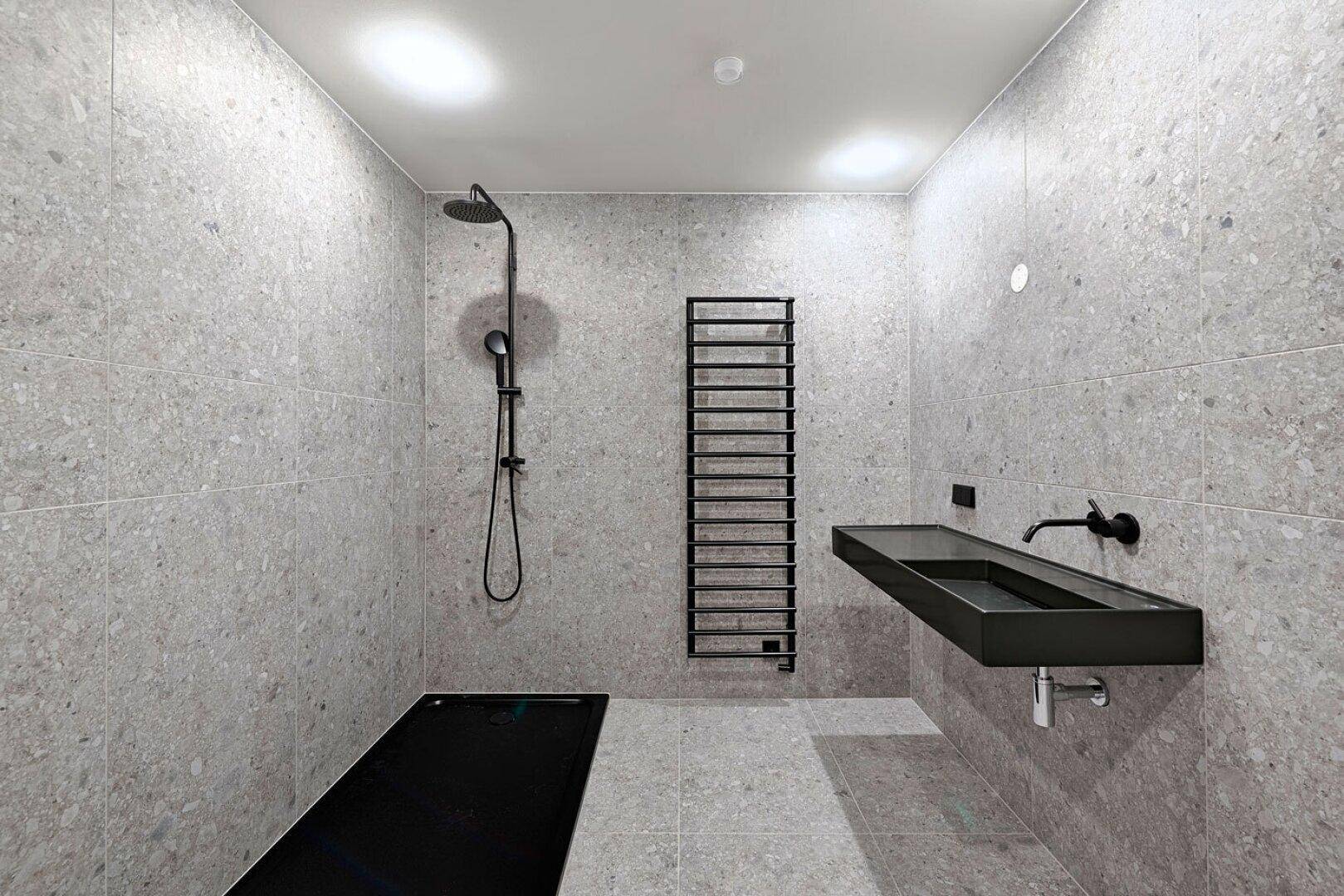 Stilvolles Badezimmer mit großer Dusche, schwarzem Waschbecken und grauen Fliesen.
