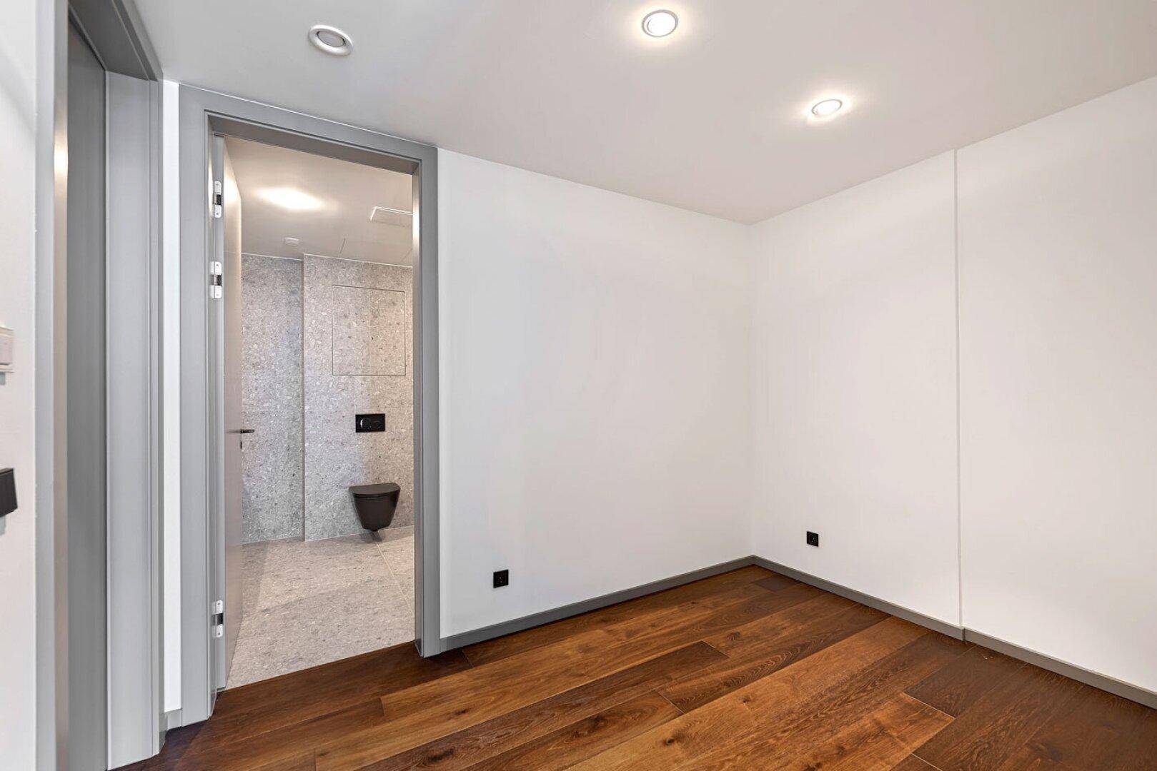 Schlafzimmer mit dunklem Holzboden und direktem Zugang zu einem modernen Badezimmer.