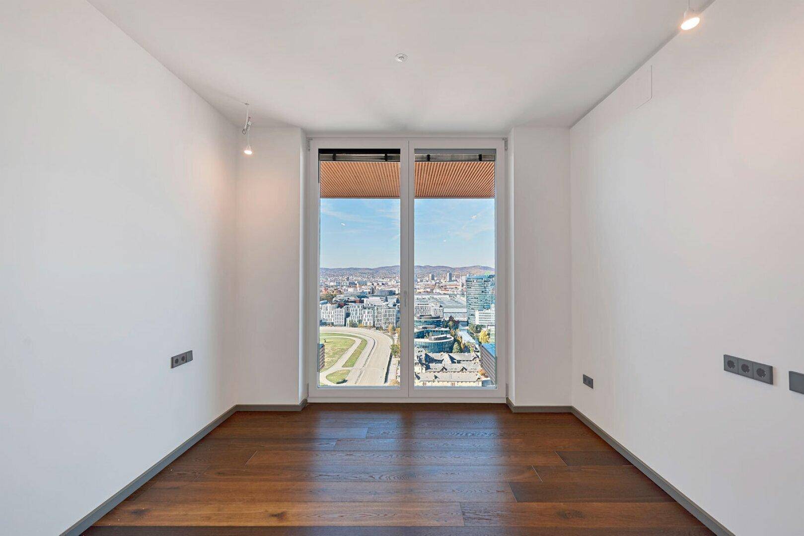 Helles Schlafzimmer mit dunklem Holzboden und großem Fenster mit Stadtblick.