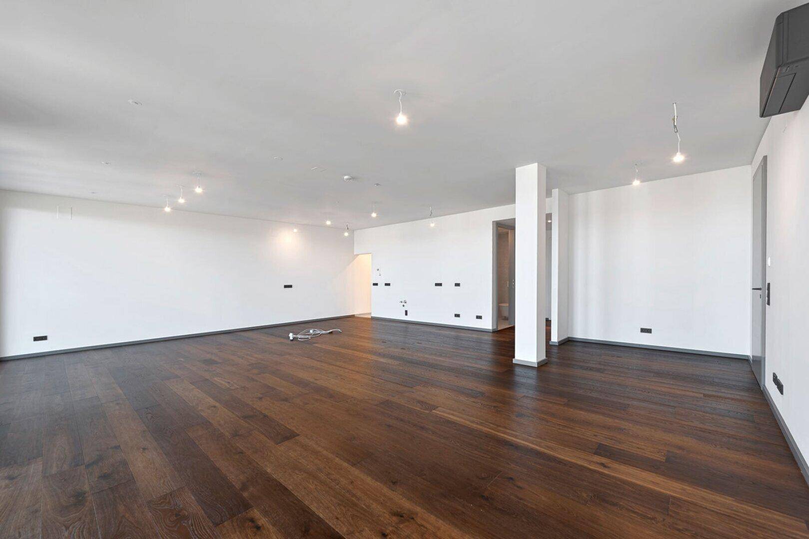 Heller, leerer Raum mit dunklem Holzboden und schlichten weißen Wänden, bereit zur Gestaltung.