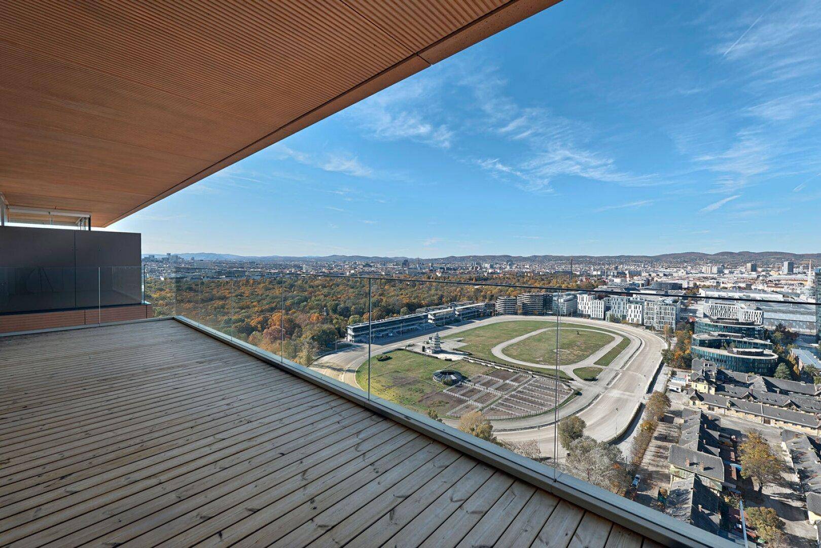 Große Holzterrasse mit weitem Blick auf grüne Flächen und die Stadt am Horizont.