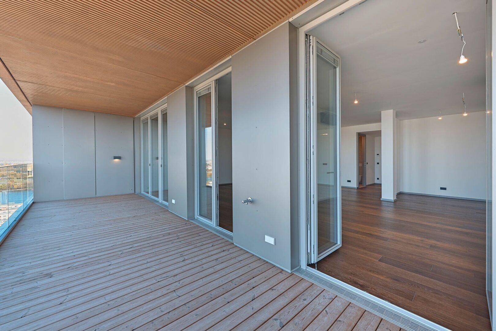 Geräumige Holzterrasse mit Glasgeländer und Zugang zu den Innenräumen der Wohnung.