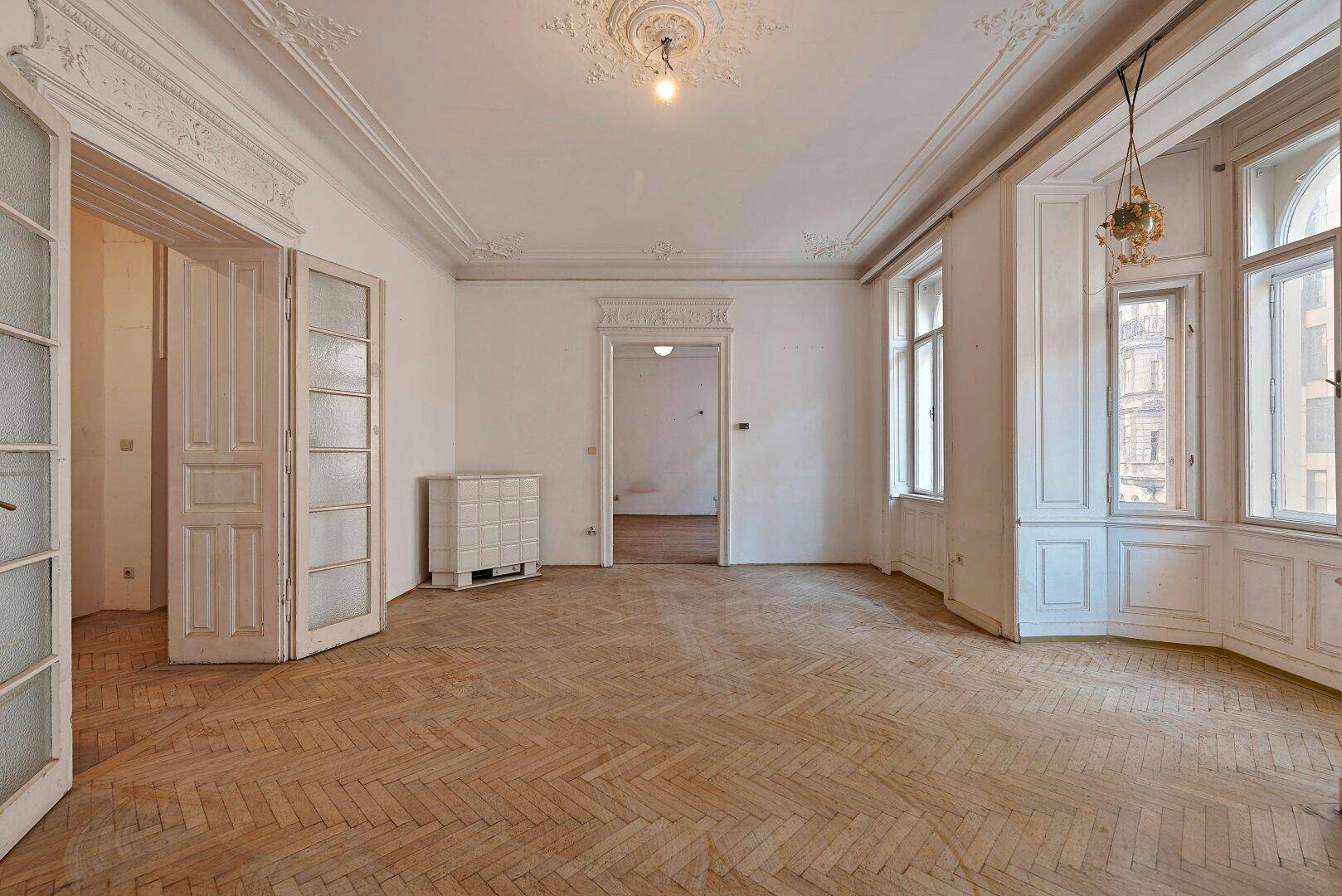 Elegantes Wohnzimmer mit Fischgrätparkett, Stuckdecken, Flügeltüren und einem hellen Erkerbereich.