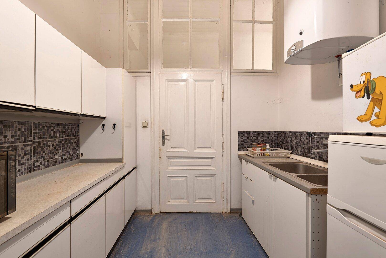 Funktionale Küche mit weißen Schränken, Mosaikfliesen, Doppelsink und einer Tür mit Oberlicht.