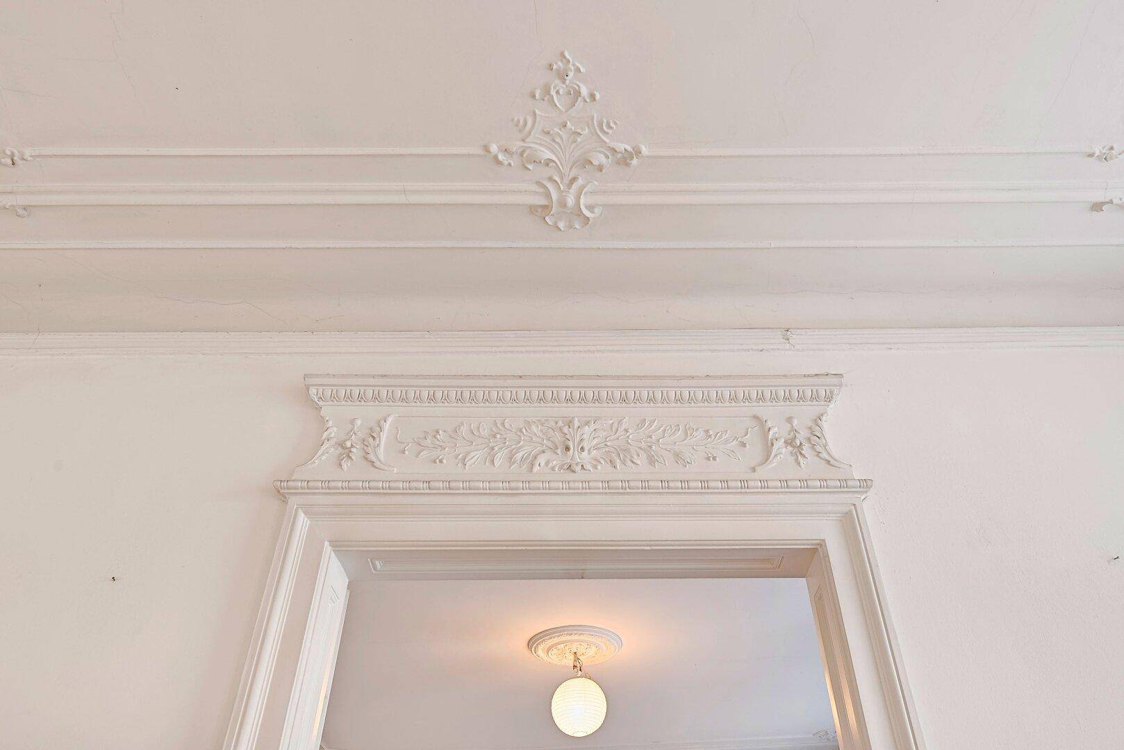 Detailaufnahme von kunstvollen Stuckverzierungen an der Decke und über einem Türrahmen.