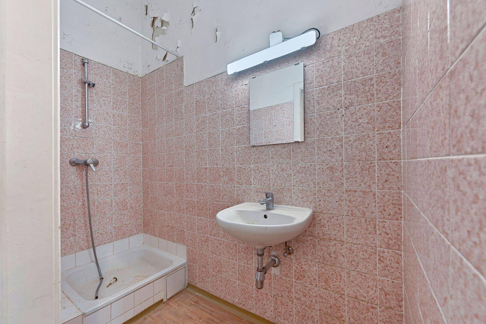 Badezimmer mit rosa Fliesen, einer Duschwanne und einem Waschbecken, das einen älteren Stil aufweist.